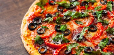 Pizza Mozzarella peyniri, salam, biber, biber, domates, zeytin, baharat ve taze fesleğen. Ahşap arka plan üzerinde İtalyan pizza