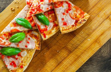 Pizza Mozzarella peyniri, jambon, domates, dilimlenmiş biber, baharatlar ve taze fesleğen. Ahşap arka plan üzerinde İtalyan pizza.