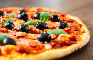 Pizza Mozzarella peyniri, salam, biber, biber, domates, zeytin, baharat ve taze fesleğen. Ahşap arka plan üzerinde İtalyan pizza