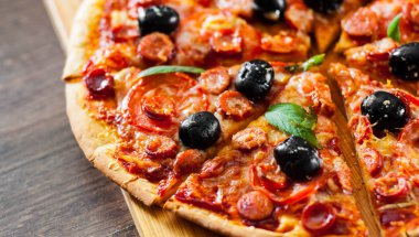 dilim Pizza Mozzarella peyniri, salam, biber, biber, domates, zeytin, baharat ve taze fesleğen. Ahşap arka plan üzerinde İtalyan pizza