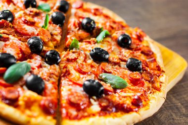 dilim Pizza Mozzarella peyniri, salam, biber, biber, domates, zeytin, baharat ve taze fesleğen. Ahşap arka plan üzerinde İtalyan pizza