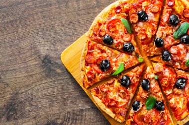 dilim Pizza Mozzarella peyniri, salam, biber, biber, domates, zeytin, baharat ve taze fesleğen. Ahşap arka plan üzerinde İtalyan pizza