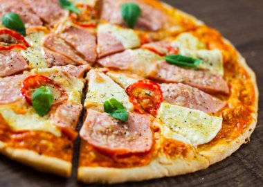 Pizza Mozzarella peyniri, jambon, domates, dilimlenmiş biber, baharatlar ve taze fesleğen. Ahşap arka plan üzerinde İtalyan pizza