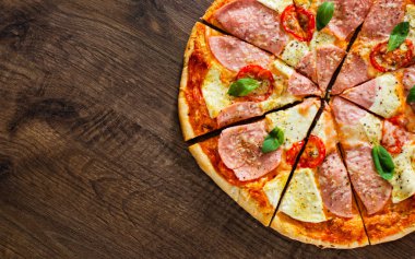 Pizza Mozzarella peyniri, jambon, domates, dilimlenmiş biber, baharatlar ve taze fesleğen. Ahşap arka plan üzerinde İtalyan pizza