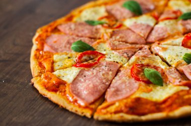 Pizza Mozzarella peyniri, jambon, domates, dilimlenmiş biber, baharatlar ve taze fesleğen. Ahşap arka plan üzerinde İtalyan pizza