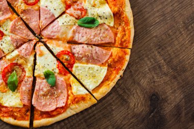 Pizza Mozzarella peyniri, jambon, domates, dilimlenmiş biber, baharatlar ve taze fesleğen. Ahşap arka plan üzerinde İtalyan pizza