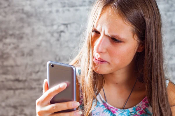 灰色の壁の背景に携帯電話を使用して長い髪の 代の若いブルネットの少女の肖像画 — ストック写真