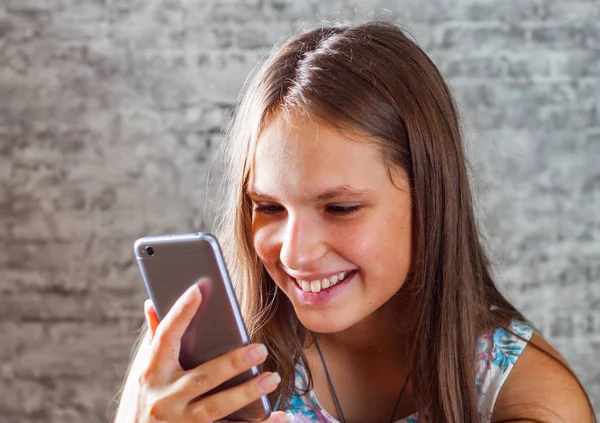 灰色の壁の背景に携帯電話を使用して長い髪の 代の若いブルネットの少女の肖像画 — ストック写真