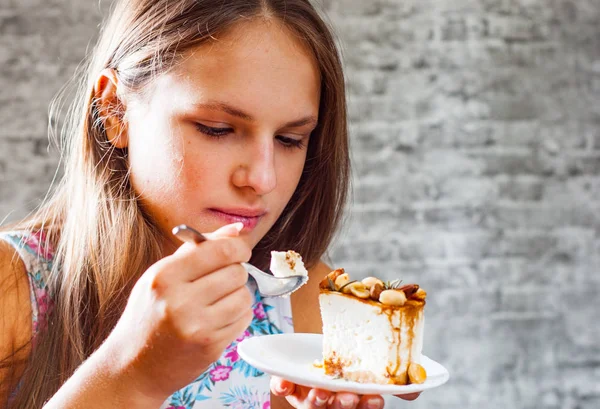 灰色の壁の背景にケーキ デザートを食べて長い髪の 代の若いブルネットの少女の肖像画 — ストック写真