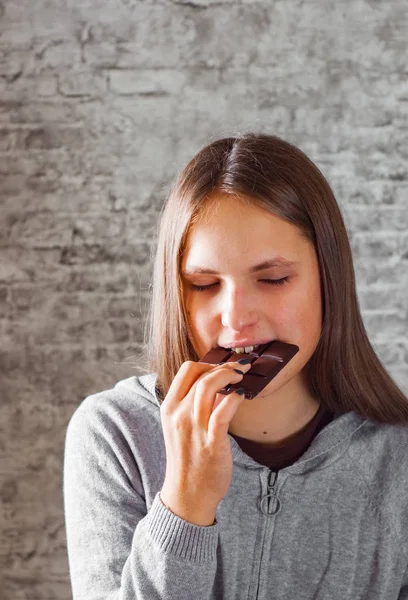 灰色の壁の背景にチョコレートを食べて長い髪の若いティーネー ジャーのブルネットの少女の肖像画 — ストック写真