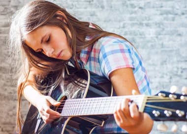 genç genç gri duvar arka plan üzerinde siyah akustik gitar çalmaya uzun saçlı esmer kız portresi