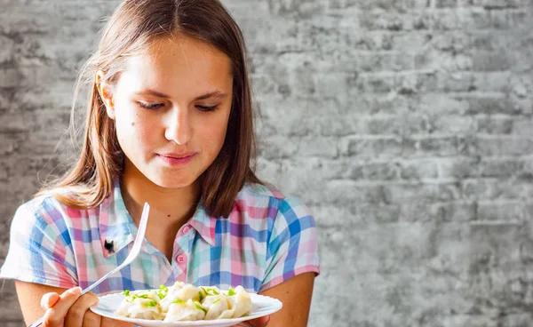 年轻的黑发女孩长头发的画像在灰色墙壁背景下吃肉饺子 — 图库照片