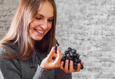 uzun saç beslenme ile genç Genç esmer kız gri duvar arka plan üzerinde üzüm portresi