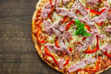 Pizza Mozzarella peyniri, jambon, biber, et, domates, baharat ve taze fesleğen. Ahşap arka plan üzerinde İtalyan pizza