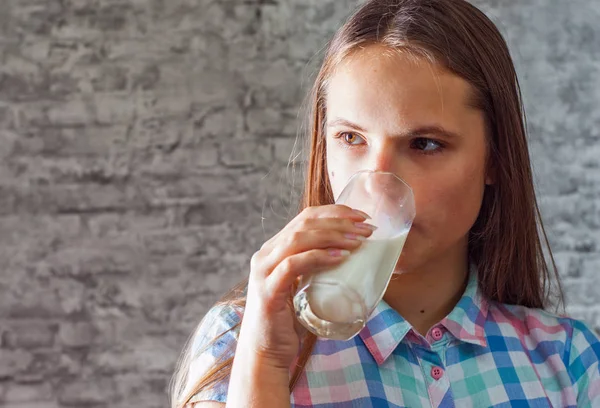 灰色の壁の背景に牛乳のガラスを保持している長い髪の若い 代のブルネットの少女の肖像画 — ストック写真