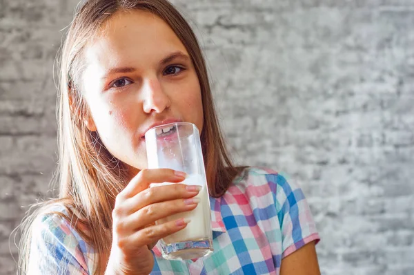 灰色の壁の背景に牛乳のガラスを保持している長い髪の若い 代のブルネットの少女の肖像画 — ストック写真