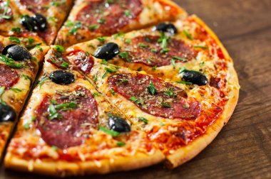 dilim Pizza Mozzarella peyniri, salam, biber, biber, zeytin, baharat ve taze fesleğen. Ahşap arka plan üzerinde İtalyan pizza