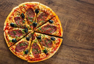 dilim Pizza Mozzarella peyniri, salam, biber, biber, zeytin, baharat ve taze fesleğen. Ahşap arka plan üzerinde İtalyan pizza