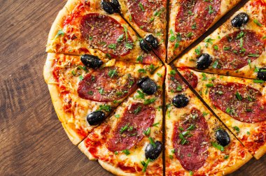 dilim Pizza Mozzarella peyniri, salam, biber, biber, zeytin, baharat ve taze fesleğen. Ahşap arka plan üzerinde İtalyan pizza