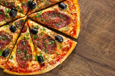 dilim Pizza Mozzarella peyniri, salam, biber, biber, zeytin, baharat ve taze fesleğen. Ahşap arka plan üzerinde İtalyan pizza