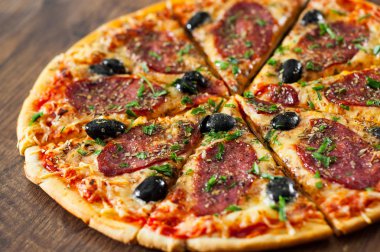 dilim Pizza Mozzarella peyniri, salam, biber, biber, zeytin, baharat ve taze fesleğen. Ahşap arka plan üzerinde İtalyan pizza