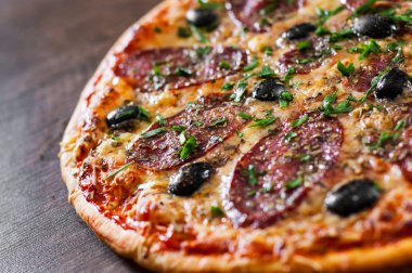 Pizza Mozzarella peyniri, salam, biber, biber, zeytin, baharat ve taze fesleğen. Ahşap arka plan üzerinde İtalyan pizza