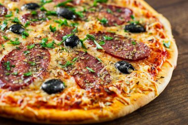 Pizza Mozzarella peyniri, salam, biber, biber, zeytin, baharat ve taze fesleğen. Ahşap arka plan üzerinde İtalyan pizza