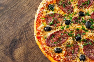 Pizza Mozzarella peyniri, salam, biber, biber, zeytin, baharat ve taze fesleğen. Ahşap arka plan üzerinde İtalyan pizza