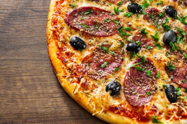 Pizza Mozzarella peyniri, salam, biber, biber, zeytin, baharat ve taze fesleğen. Ahşap arka plan üzerinde İtalyan pizza