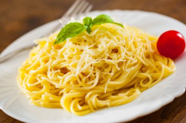 spagetti makarna ahşap masa üzerinde beyaz tabakta rendelenmiş peynir ile