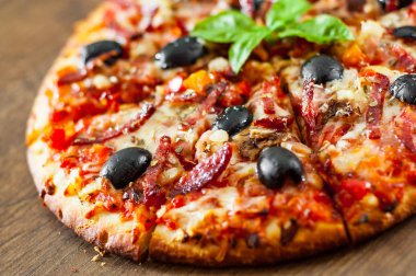 dilim Pizza Mozzarella peyniri, salam, biber, jambon, biber, zeytin, baharat ve taze fesleğen. Ahşap arka plan üzerinde İtalyan pizza