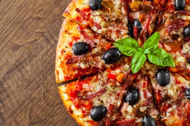 dilim Pizza Mozzarella peyniri, salam, biber, jambon, biber, zeytin, baharat ve taze fesleğen. Ahşap arka plan üzerinde İtalyan pizza