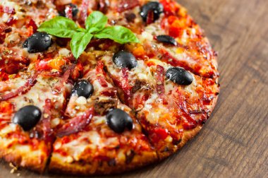 dilim Pizza Mozzarella peyniri, salam, biber, jambon, biber, zeytin, baharat ve taze fesleğen. Ahşap arka plan üzerinde İtalyan pizza