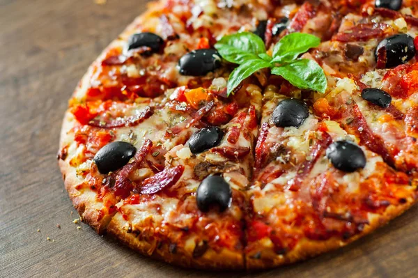 dilim Pizza Mozzarella peyniri, salam, biber, jambon, biber, zeytin, baharat ve taze fesleğen. Ahşap arka plan üzerinde İtalyan pizza