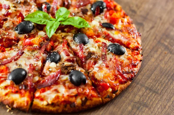 dilim Pizza Mozzarella peyniri, salam, biber, jambon, biber, zeytin, baharat ve taze fesleğen. Ahşap arka plan üzerinde İtalyan pizza