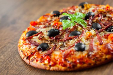 Pizza Mozzarella peyniri, salam, biber, jambon, biber, zeytin, baharat ve taze fesleğen. Ahşap arka plan üzerinde İtalyan pizza