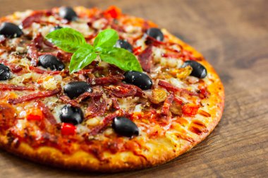 Pizza Mozzarella peyniri, salam, biber, jambon, biber, zeytin, baharat ve taze fesleğen. Ahşap arka plan üzerinde İtalyan pizza