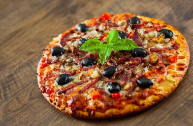 Pizza Mozzarella peyniri, salam, biber, jambon, biber, zeytin, baharat ve taze fesleğen. Ahşap arka plan üzerinde İtalyan pizza