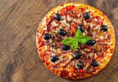 Pizza Mozzarella peyniri, salam, biber, jambon, biber, zeytin, baharat ve taze fesleğen. Ahşap arka plan üzerinde İtalyan pizza
