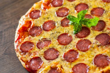 Mozzarella peyniri, salam, domates sosu, biber, baharat ve taze fesleğen ile biberli Pizza. Ahşap arka plan üzerinde İtalyan pizza