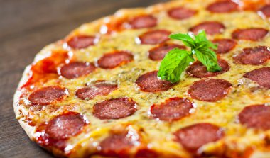 Mozzarella peyniri, salam, domates sosu, biber, baharat ve taze fesleğen ile biberli Pizza. Ahşap arka plan üzerinde İtalyan pizza