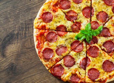 Mozzarella peyniri, salam, domates sosu, biber, baharat ve taze fesleğen ile biberli Pizza. Ahşap arka plan üzerinde İtalyan pizza