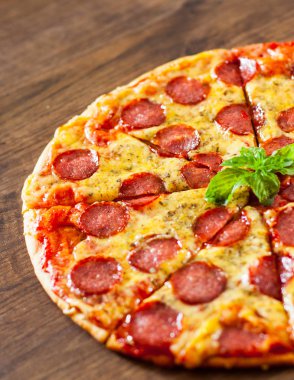 Mozzarella peyniri, salam, domates sosu, biber, baharat ve taze fesleğen ile biberli Pizza. Ahşap arka plan üzerinde İtalyan pizza