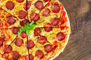 Mozzarella peyniri, salam, domates sosu, biber, baharat ve taze fesleğen ile biberli Pizza. Ahşap arka plan üzerinde İtalyan pizza