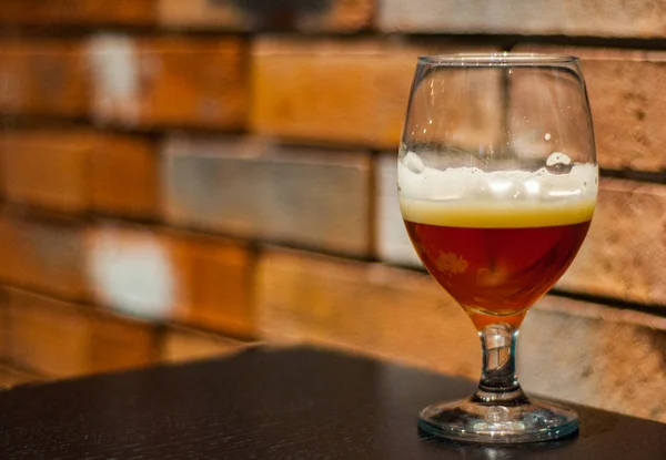 Close up on a glass of amber Pale Ale beer on wooden table in bar on brick wall background with copy space.