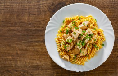 Ahşap masa üzerinde beyaz plaka Düdük makarna ile krem soslu kızarmış tavuk fileto dilimlenmiş