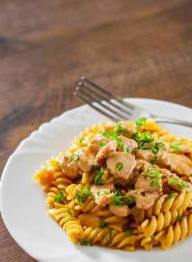 Ahşap masa üzerinde beyaz plaka Düdük makarna ile krem soslu kızarmış tavuk fileto dilimlenmiş