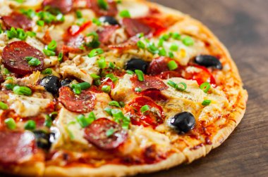 Tavuk eti, Mozzarella peyniri, sucuk, domates, zeytin, salam pizza. Ahşap arka plan üzerinde İtalyan pizza