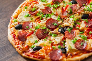 Tavuk eti, Mozzarella peyniri, sucuk, domates, zeytin, salam pizza. Ahşap arka plan üzerinde İtalyan pizza