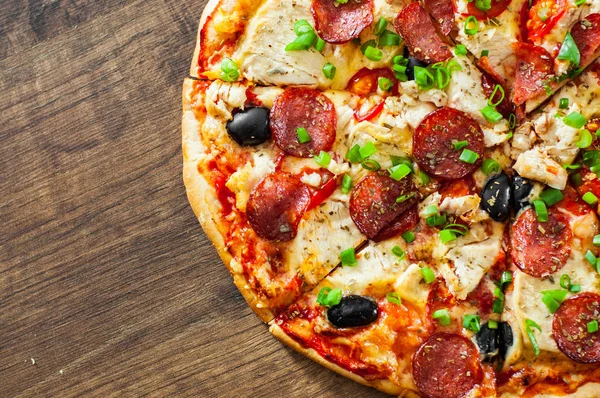 Tavuk eti, Mozzarella peyniri, sucuk, domates, zeytin, salam pizza. Ahşap arka plan üzerinde İtalyan pizza